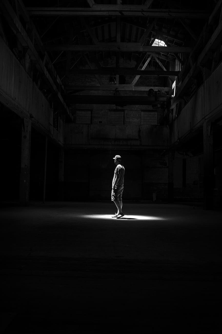 man standing on the light, grayscale photo of person standing in middle of empty building with light passing through its roof