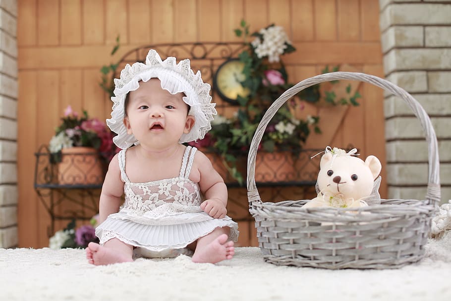 baby wearing white floral dress sitting beside gray basket with white teddy bear inside on fleece mat, HD wallpaper