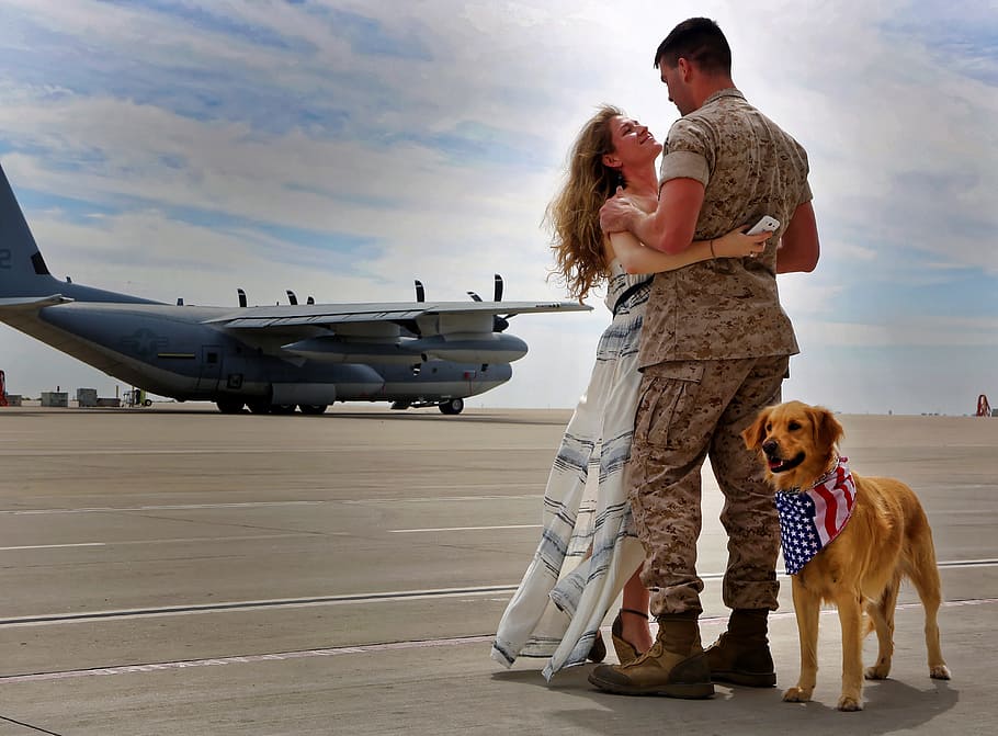 golden retriever standing next to woman and man hugging, army