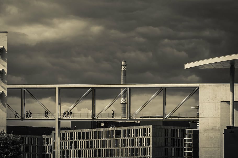 grayscale photography of people crossing on bridge between buildings HD wallpaper