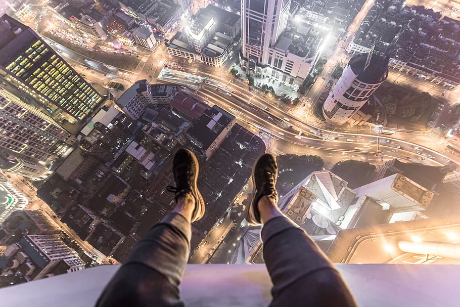 A man sitting on the roof of a city building with his feet and shoes hanging over the edge, HD wallpaper