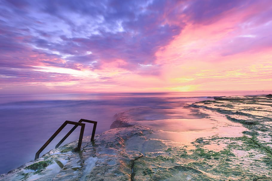 wet grass field with railing bars and ocean view with cloudy sky during daytime HD wallpaper