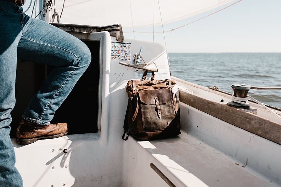 person in blue denim jeans on yacht beside brown bag, brown leather knapsack in white speedboat beside a person HD wallpaper
