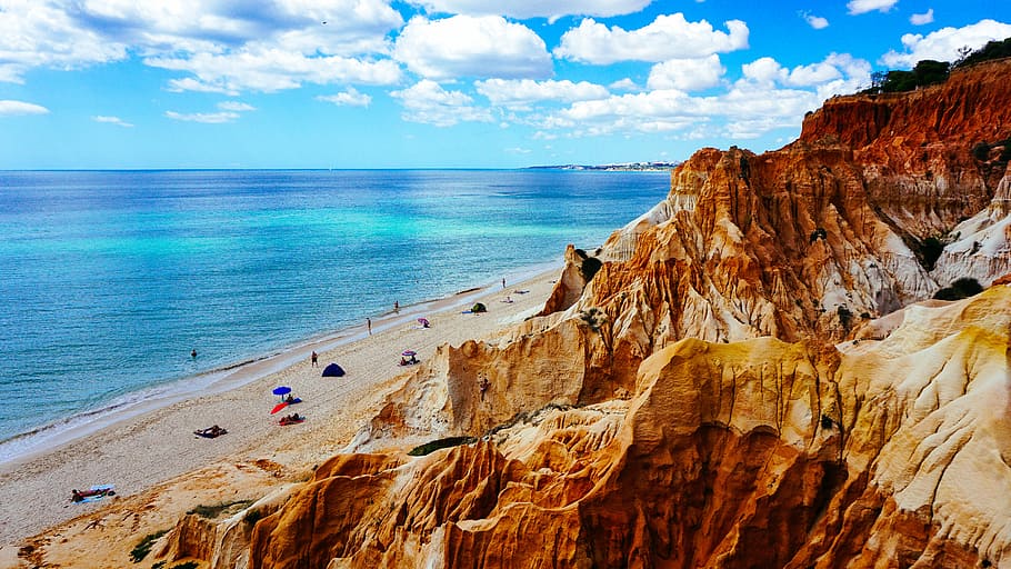 landscape photography of rock formation near body of water, rock formation mountain beside ocean under white clouds and blue sky HD wallpaper