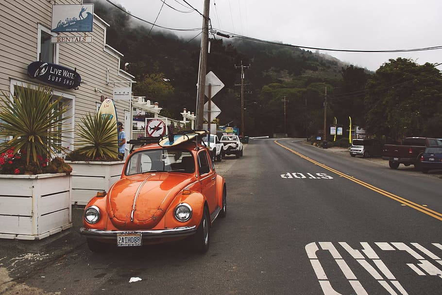 orange Volkswagen Beetle coupe on road near brown building, vw