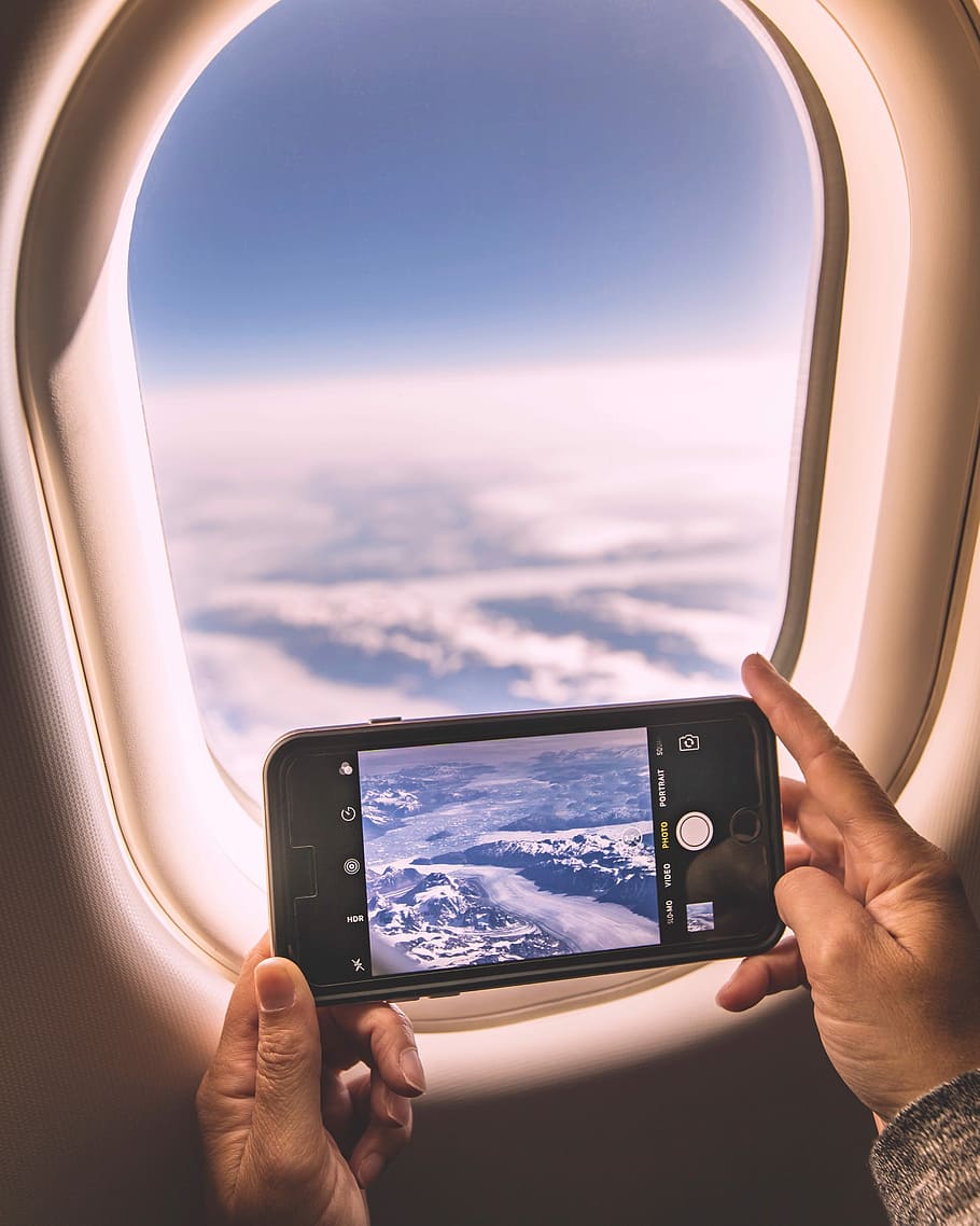 selective focus photography of person holding iPhone while taking photo of sky, person in airplane using iPhone capturing clouds during daytime HD wallpaper