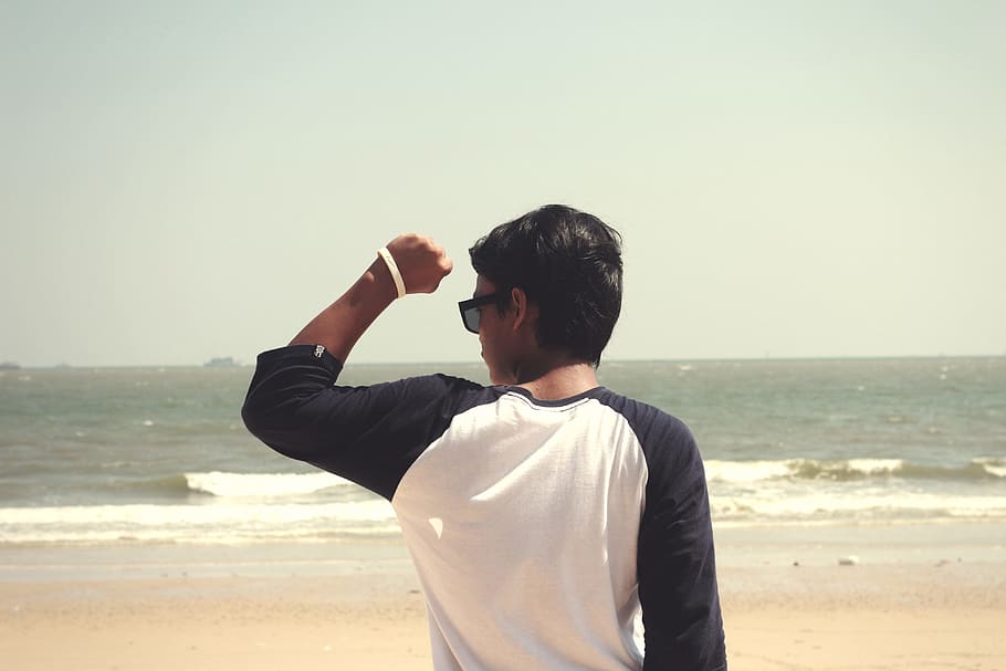 Man in White and Black Raglan Shirt Standing in the Seashore at Daytime HD wallpaper