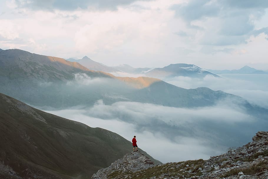 man standing on mountain edge during daytime, person standing on gray rock formation's top facing vast foggy mountains during daytime photo HD wallpaper