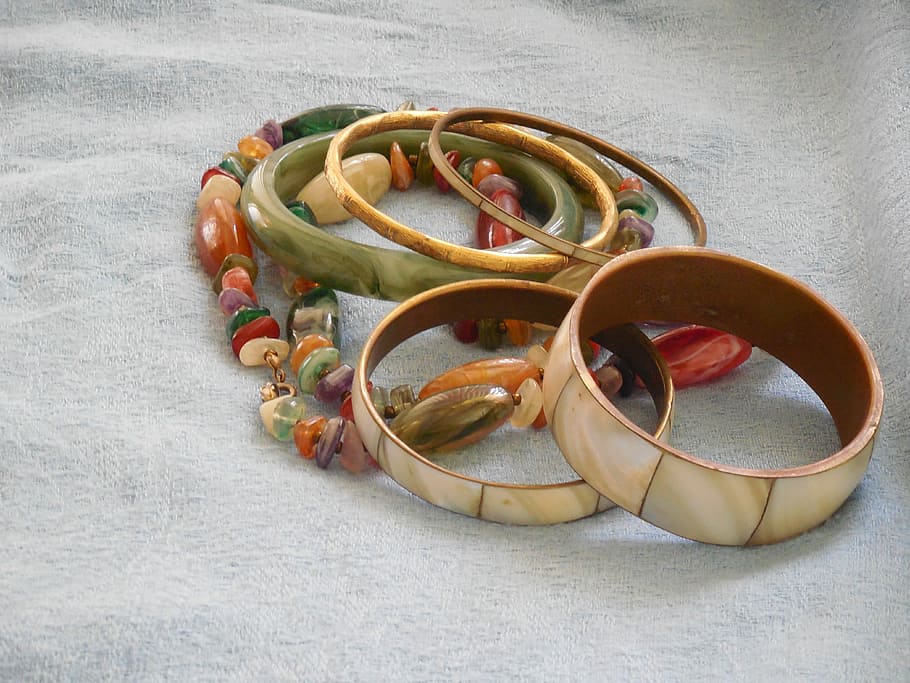five ceramic bangles above multi-colored beaded necklace in gray textile
