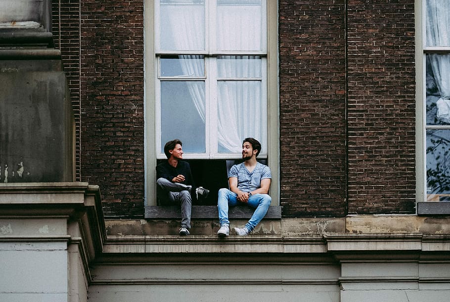 two men sitting on windowpane mantle, two man sitting on building window