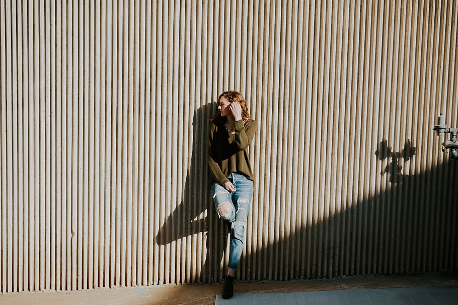 woman leaning on beige wall with shadow at daytime, woman leaning with one foot on wall during daytime