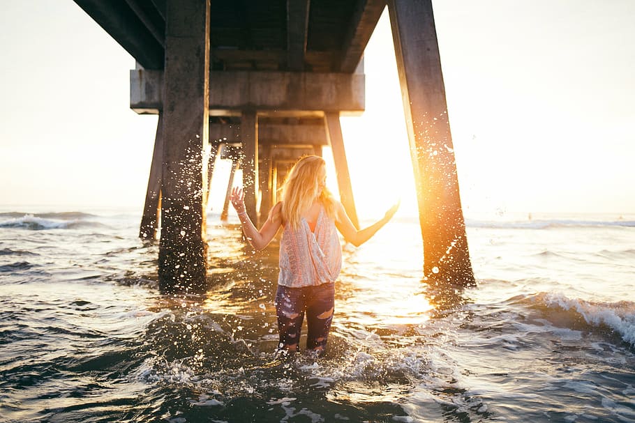 woman wearing white shirt standing on blue body of water under bridge during daytime HD wallpaper