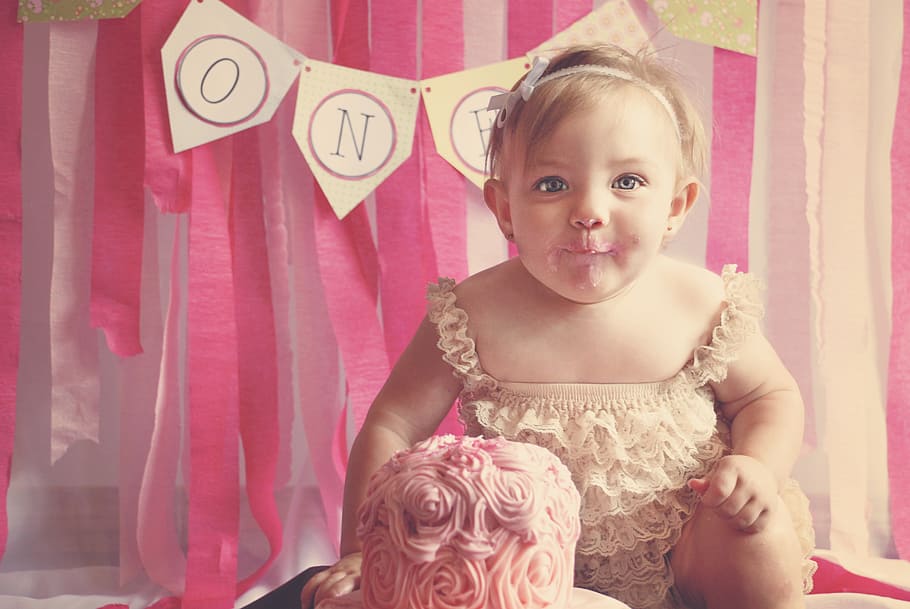 baby's white sleeveless dress sitting in front of cake, first birthday