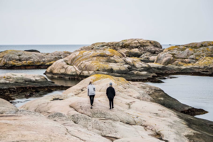 woman and man walking on rock formation near body of water during daytime, two men waling on rock near body of water HD wallpaper
