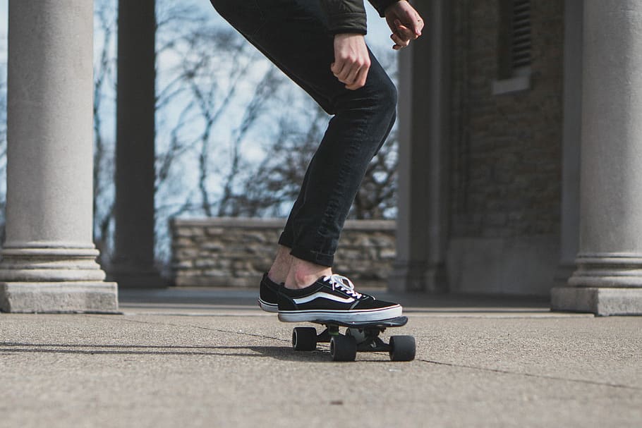 man skate boarding, person wearing black VANS Old Skool shoes riding skateboard