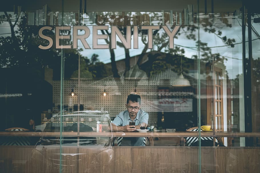 man holding smartphone sitting beside table inside cafe, shallow focus photography of a man using device, HD wallpaper