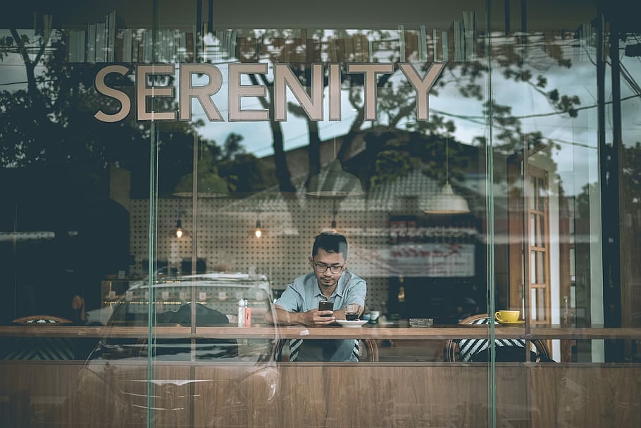 man holding smartphone sitting beside table inside cafe, shallow focus photography of a man using device HD wallpaper