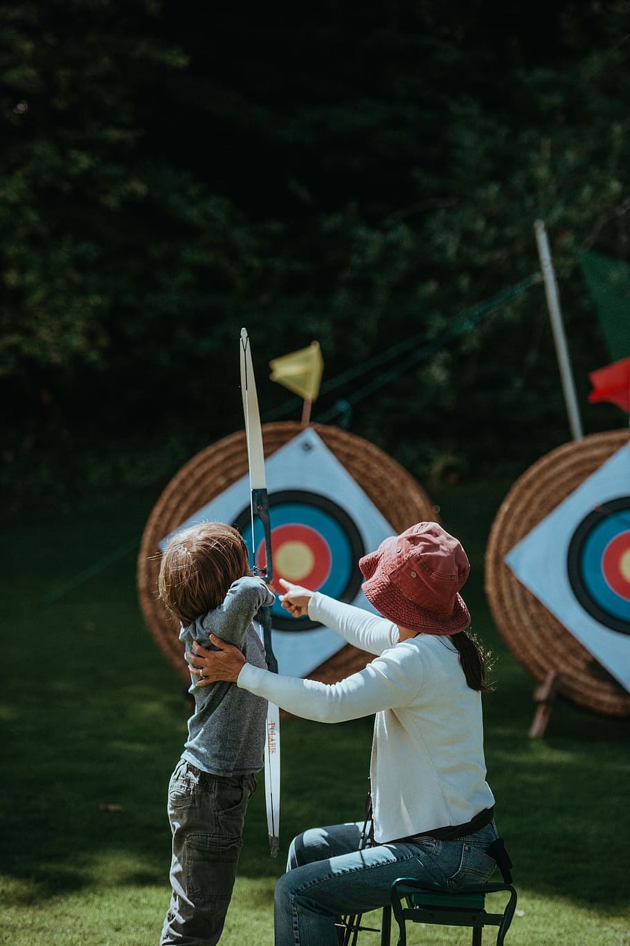 Child learning archery, woman teaching toddler to shoot arrow HD wallpaper