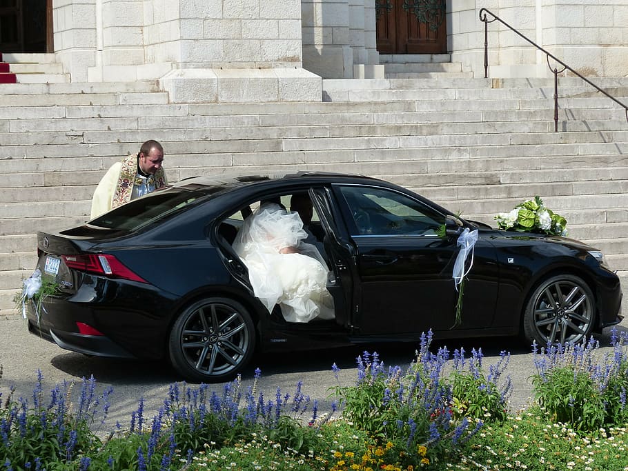 woman wearing wedding dress getting out of black sedan at daytime