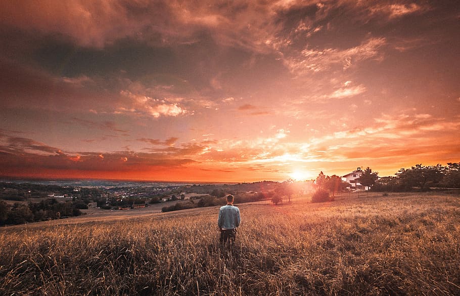 man standing on grass field during golden hour, sunset, hills