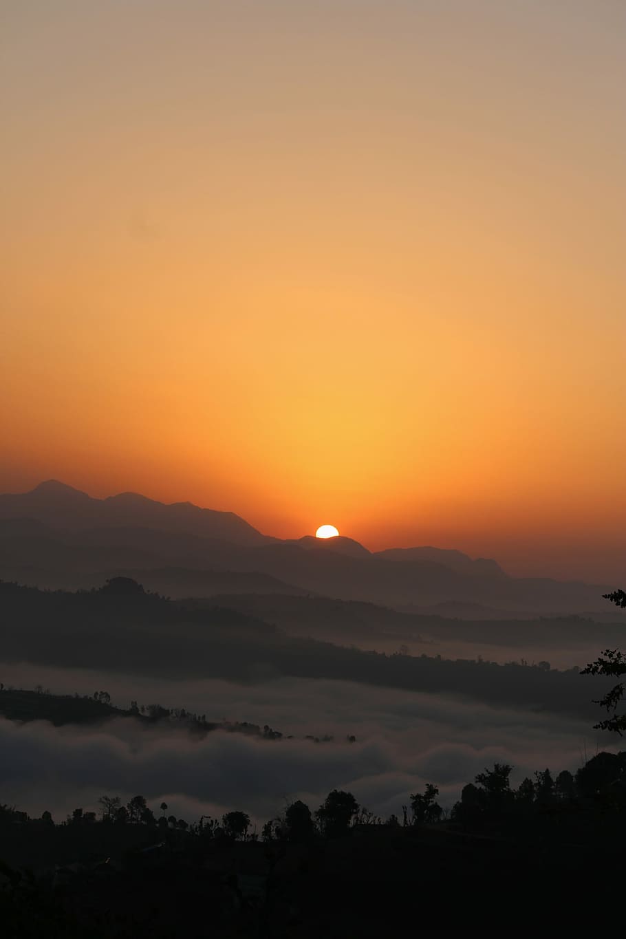 sun peeping on ice mountain, silhouette of trees covered with clouds and mountain in distance during golden hour HD wallpaper