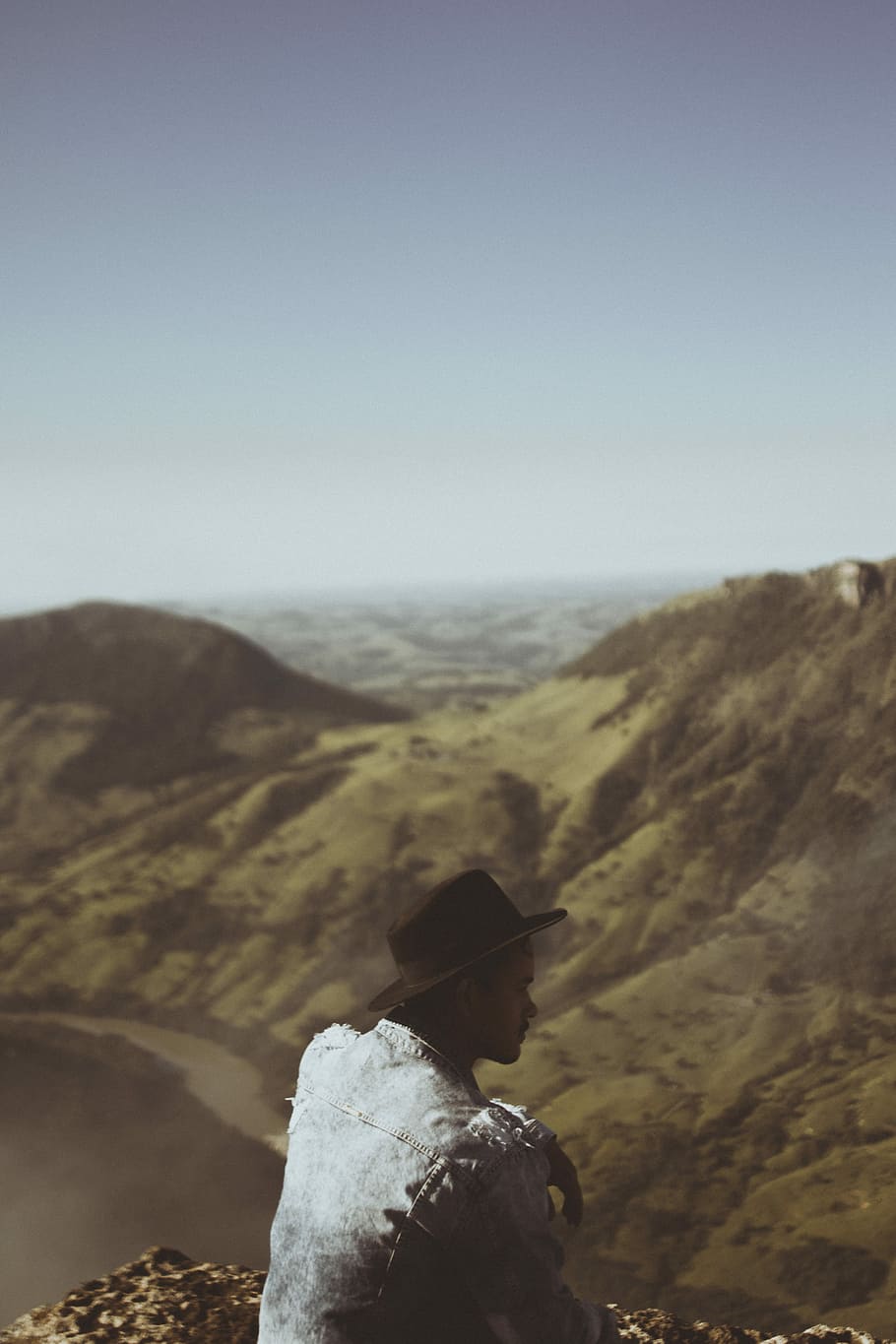 person on top of mountain, man sitting on rock formation near body of water HD wallpaper
