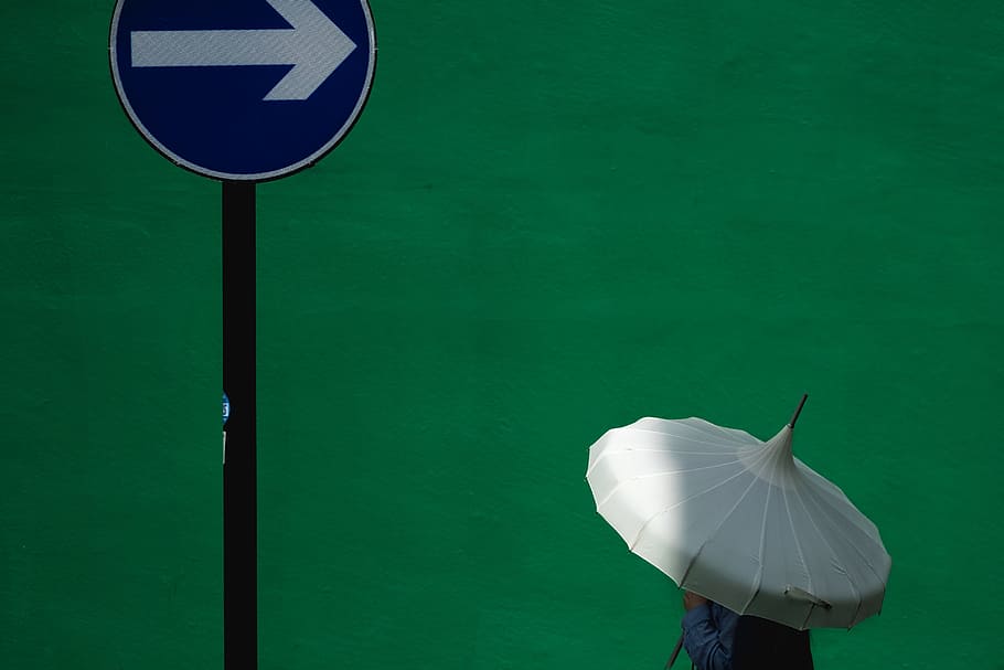 person using white umbrella near blue road signage, man holding white umbrella nearly on road sign