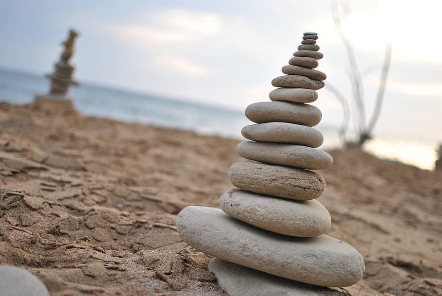 stacked stones on gray sand near body of water under white clouds during daytime HD wallpaper