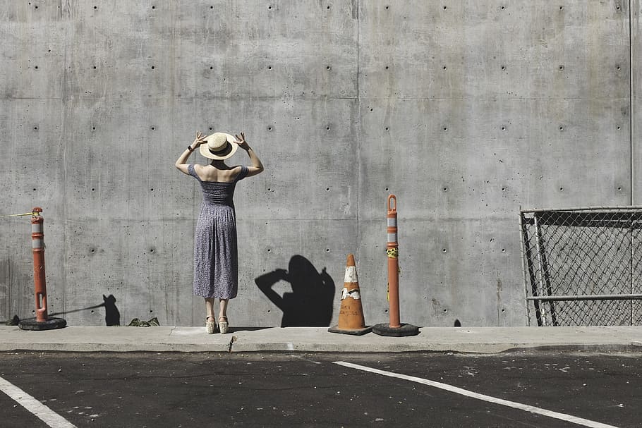 woman in gray dress facing a wall, woman wearing white sunhat and gray dress