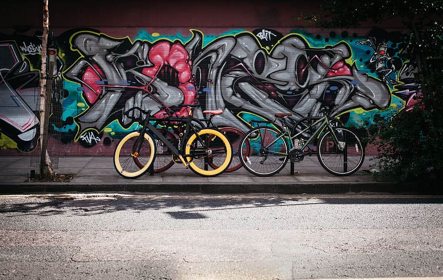 two black and and yellow bikes near wall with graffiti, art, bicycles