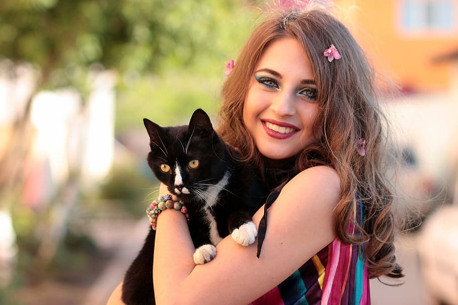 focus photography of woman carrying tuxedo cat during daytime