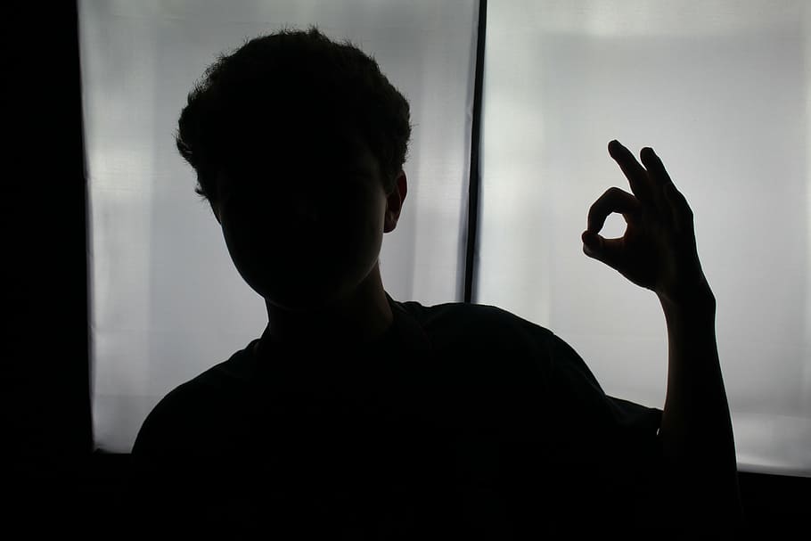 boy gesturing ok near glass window, sillhouette, black and white