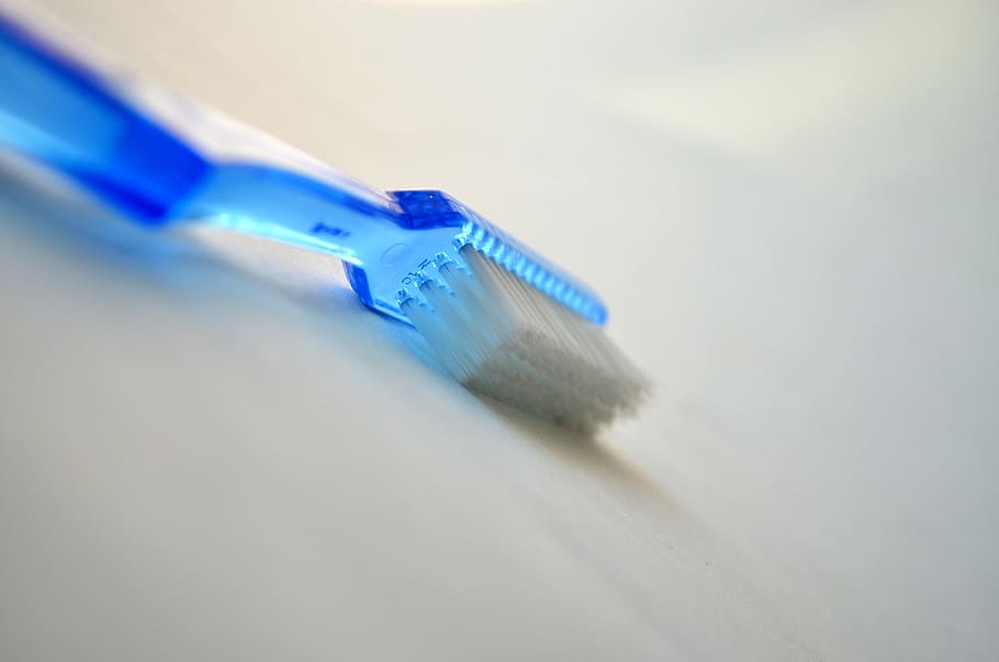 blue plastic white bristle toothbrush on white surface, dental care