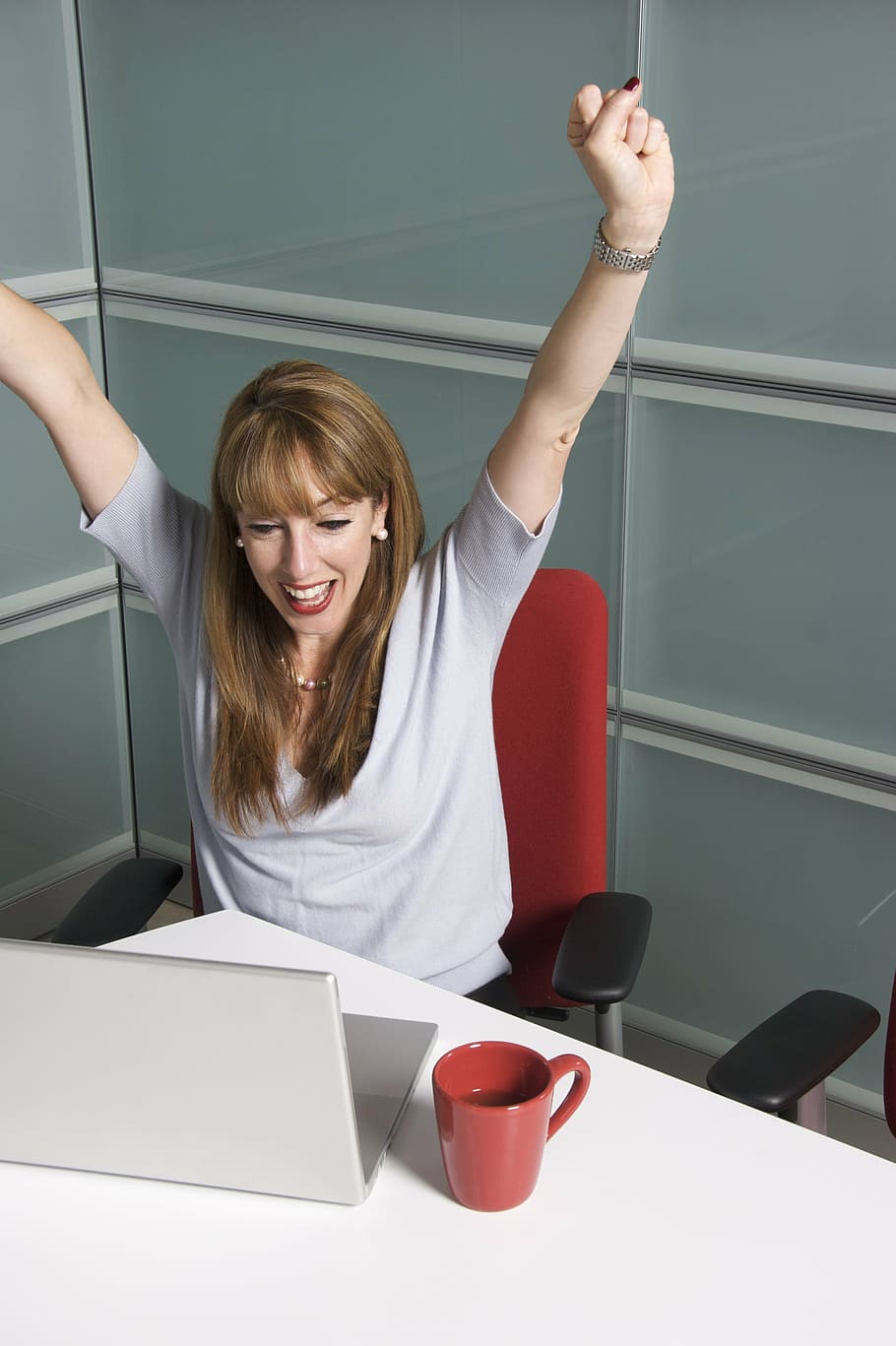 woman sitting on office chair front of laptop raising hands, female