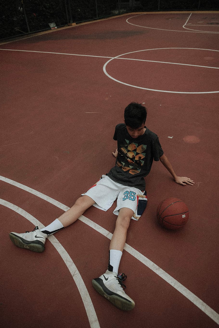 man lying on basketball court looking to basketball, man sitting on basketball court beside basketball