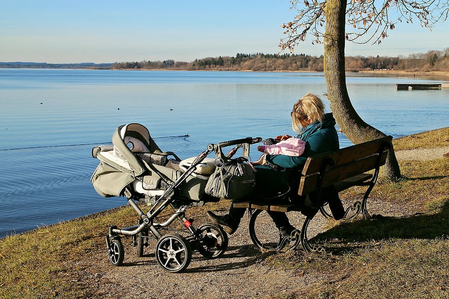 woman sitting on bench with stroller located near the body of water