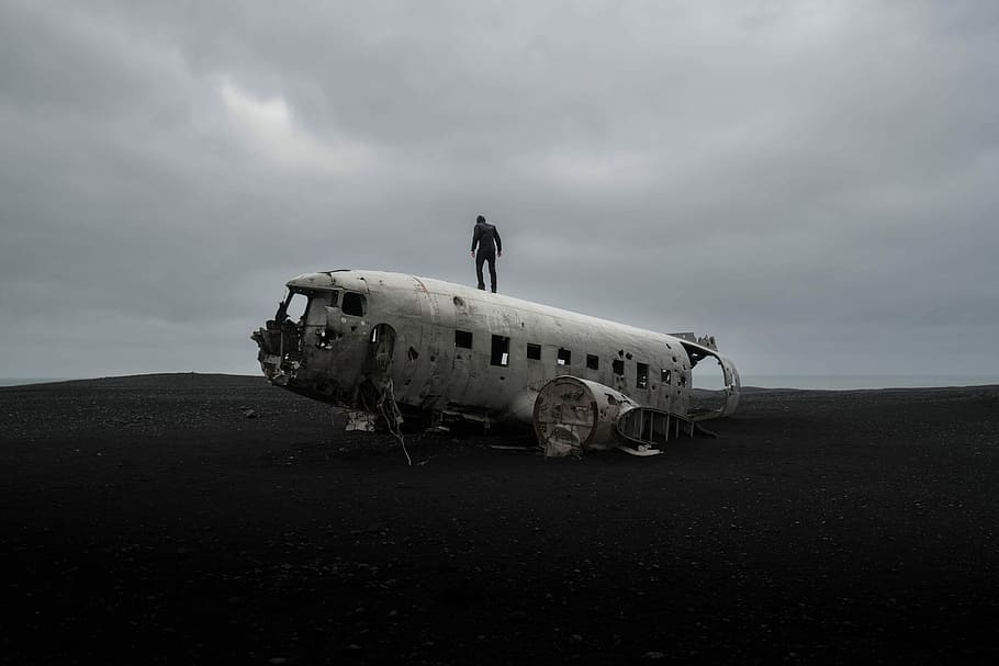 person standing on wrecked airplane under gloomy sky, silhouette of man standing on abandoned plane during daytime HD wallpaper