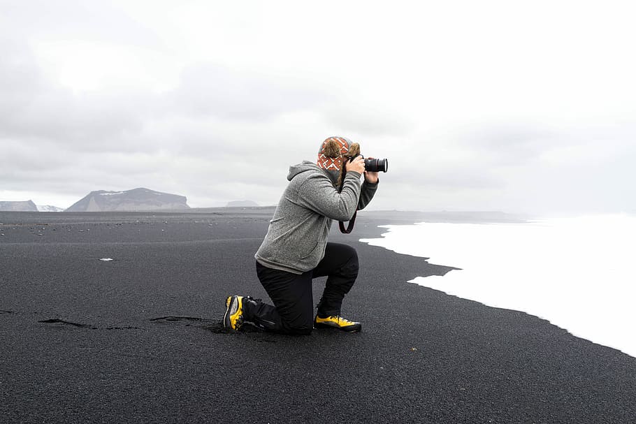 person in gray fleece hoodie on seashore taking a photo while facing the sea HD wallpaper