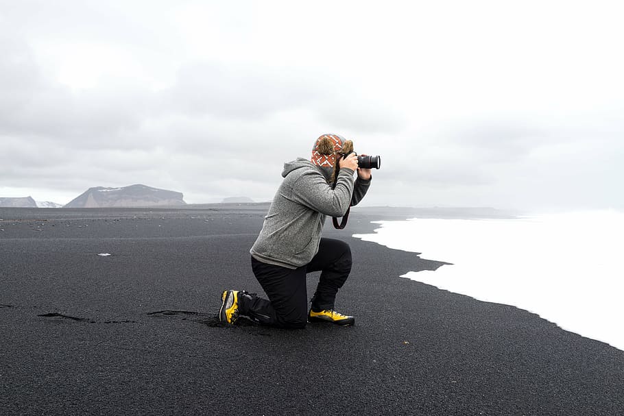 man in gray hoodie holding DSLR camera on beach shore during fog