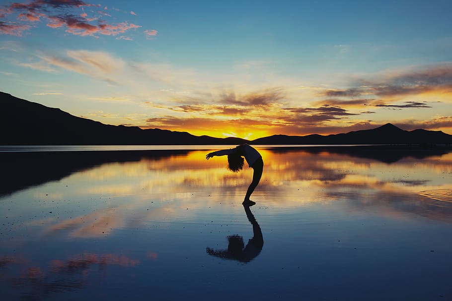 silhouette photo of person bending on body of water against orange sky HD wallpaper