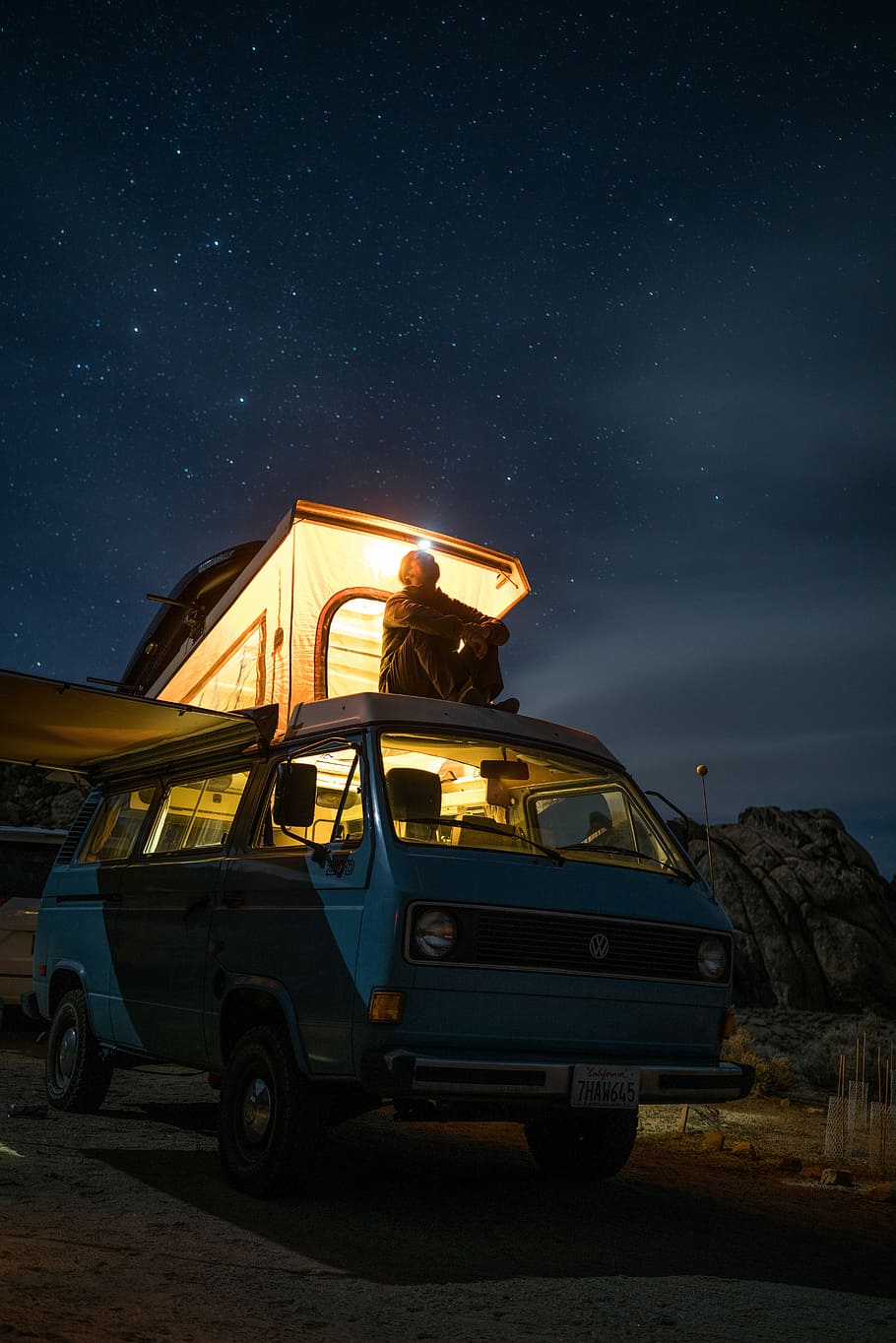 man sitting on top of blue van staring at sky during nighttime, person sitting on top of teal van with camping trailer during nighttime HD wallpaper