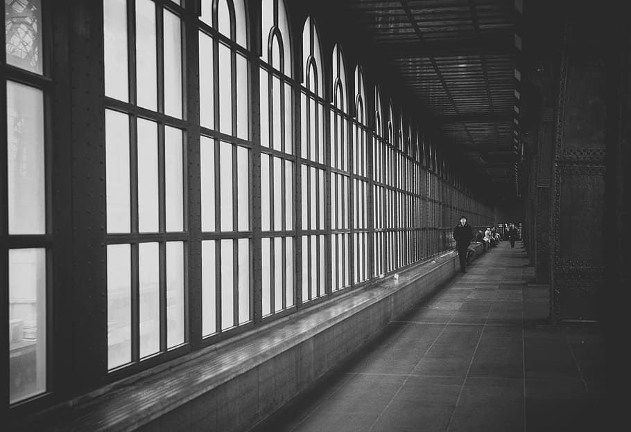 grayscale photo of man walking on hallway near glass window HD wallpaper
