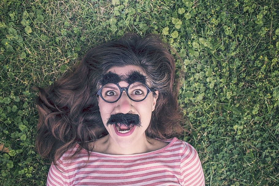 woman with fake mustache and eyebrow lying on green grass, grimace HD wallpaper