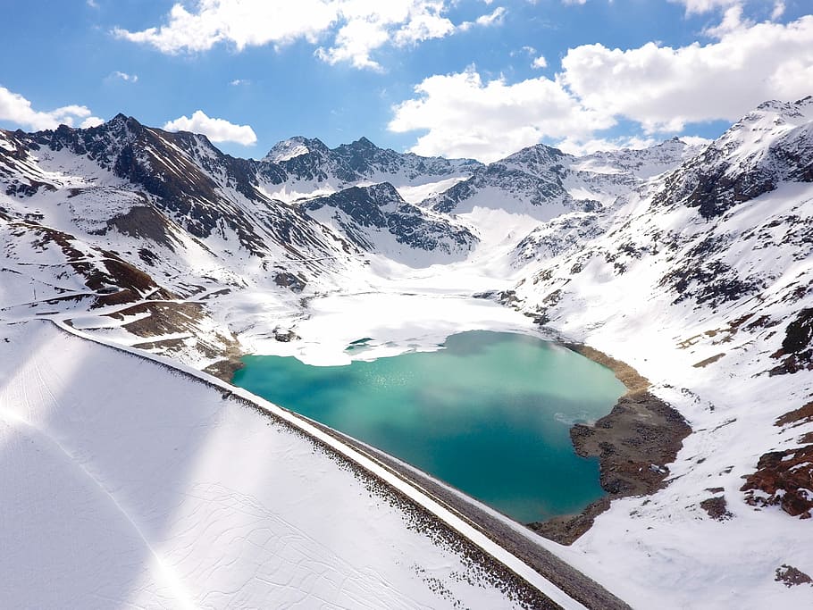aerial view of body of water, lake between snow capped mountain under white clouds during daytie HD wallpaper