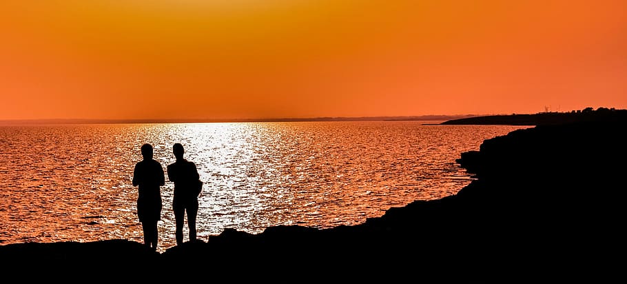silhouette of two person standing near body of water, sunset HD wallpaper
