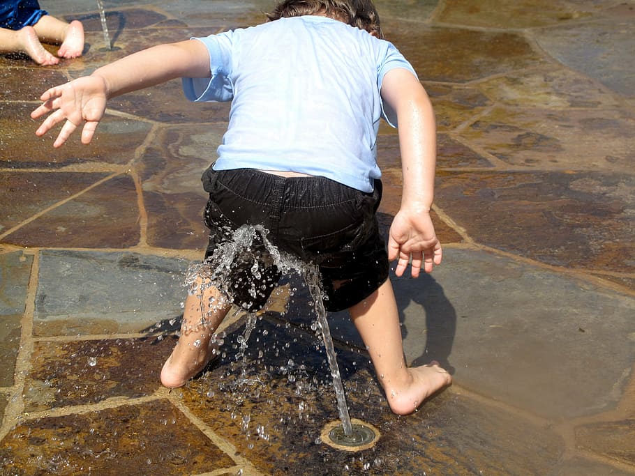 infant in black shorts playing with water sprinkler, splashing.