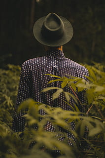 man standing near green leafed plants during daytime, person wearing black cowboy hat and black and white dress shirt standing and surrounded by green plants HD wallpaper