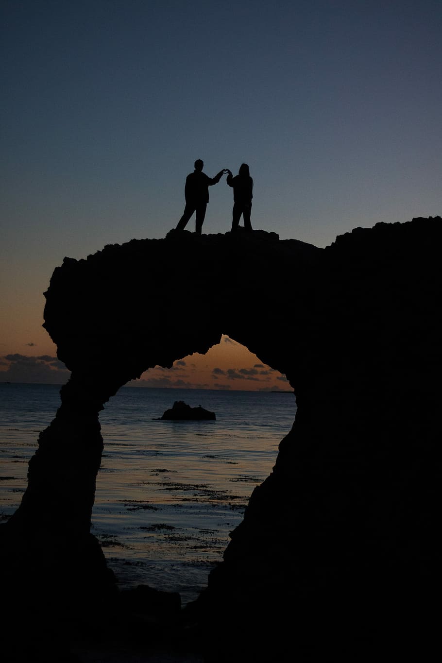 silhouette of two persons atop a rock formation near the ocean, silhouette of couple on top of arch HD wallpaper