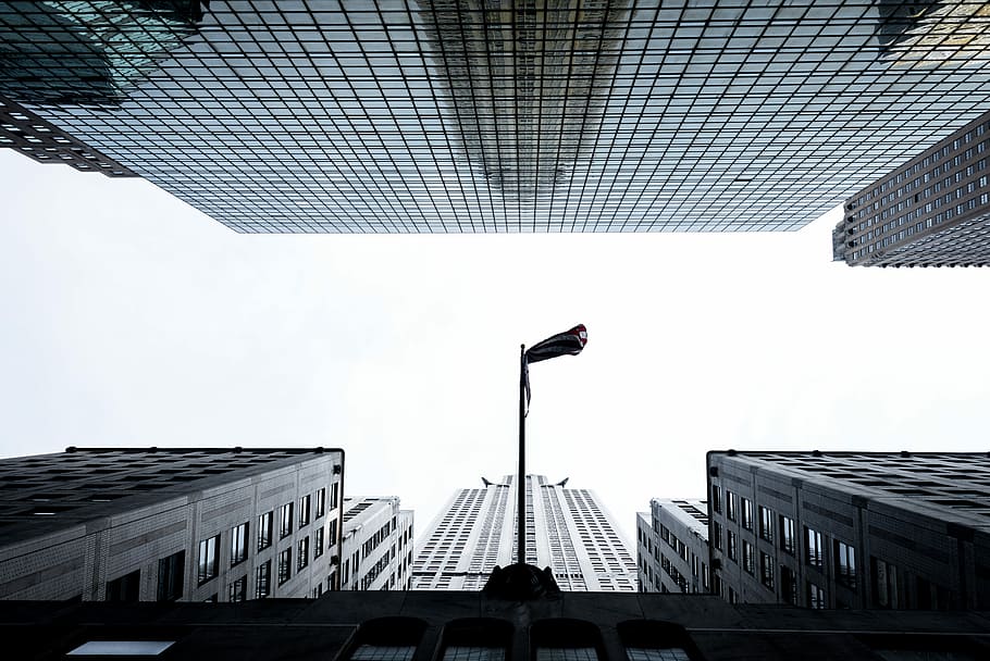 white concrete building under clear sky during daytime, low angle view photography of flag pole between high-rise buildings HD wallpaper