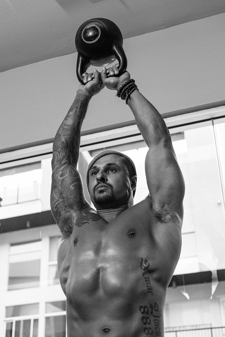 grayscale photo of man holding kettlebell, man lifting black kettle bell in grayscale photography